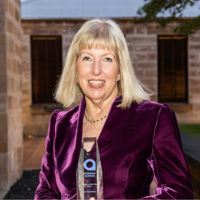 Woman smiling at camera with purple velvet jacket, blonde hair to shoulders, golding a trophy