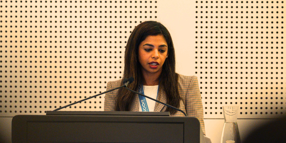 Female with long dark hair speaking from a podium