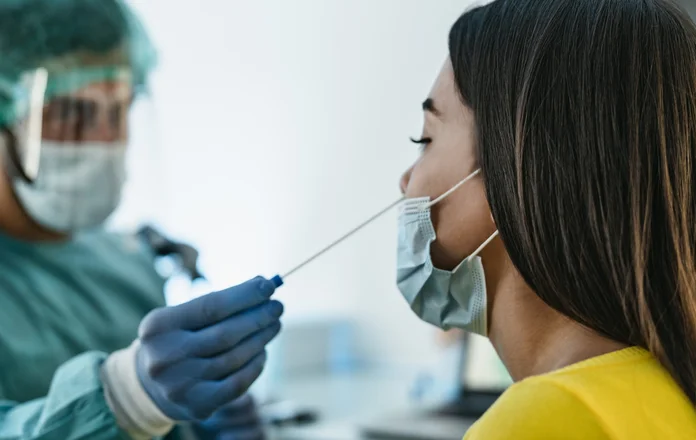 Medical worker wearing personal protective equipment doing corona virus swab on female patient.