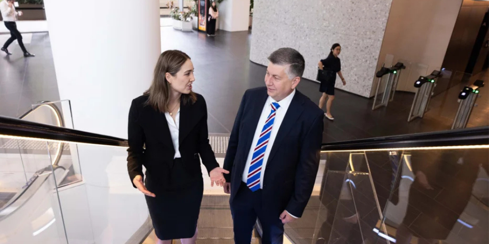 Two professionals in business attire having a conversation on an escalator in a modern office building.