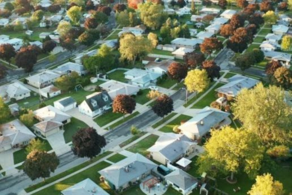 Suburbs arial shot with white roofs and green trees