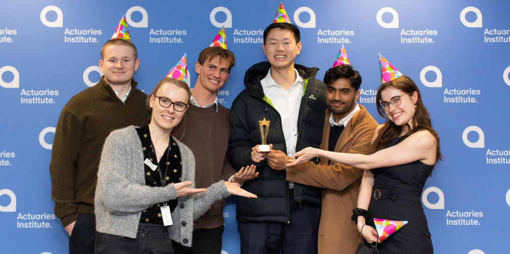 Group of young people in party hats celebrating with their winner trophy in front of a media banner