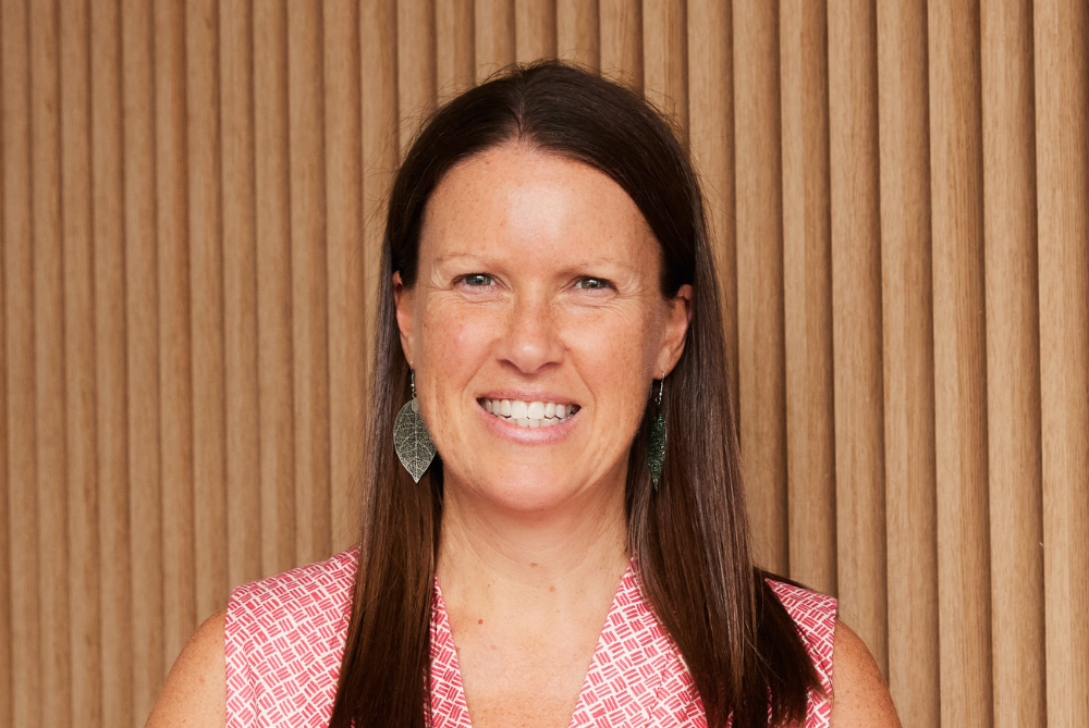 Women portrait photo with brown hair past shoulders, smiling with light red and white checked sleeveless dress.