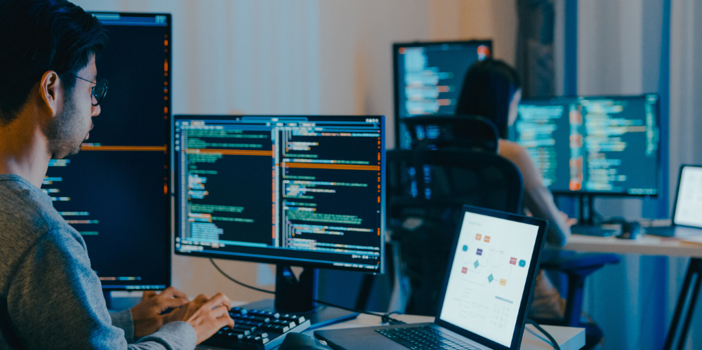 A worker typing in code on various screens