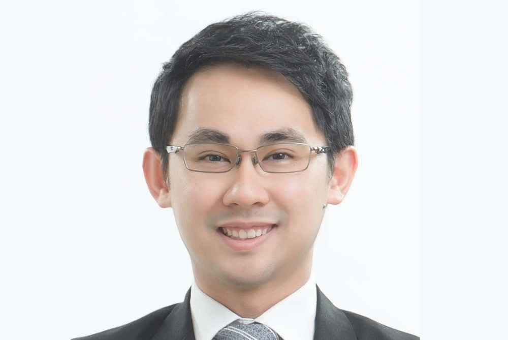 Head and shoulders photo of a business man with black hair, and glasses. Suit with white shirt and striped grey tie on white background.
