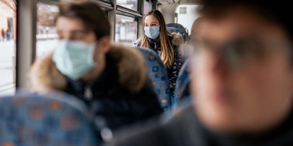 Young girl is wearing sterile face mask because of the new Coronavirus COVID-19. She is sitting on a bus. She is looking outside the window.