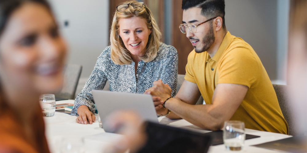 Two professionals - one man and one women - collaborating together on a laptop. 