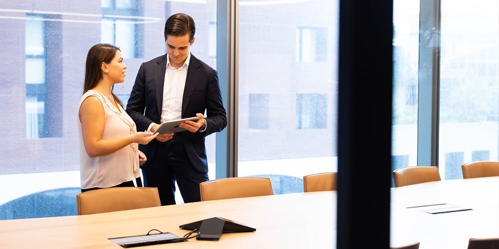 A woman and a man in a meeting room discussing something on an iPad