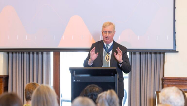 Conference speaker with medal on, explaining something with hand gestures