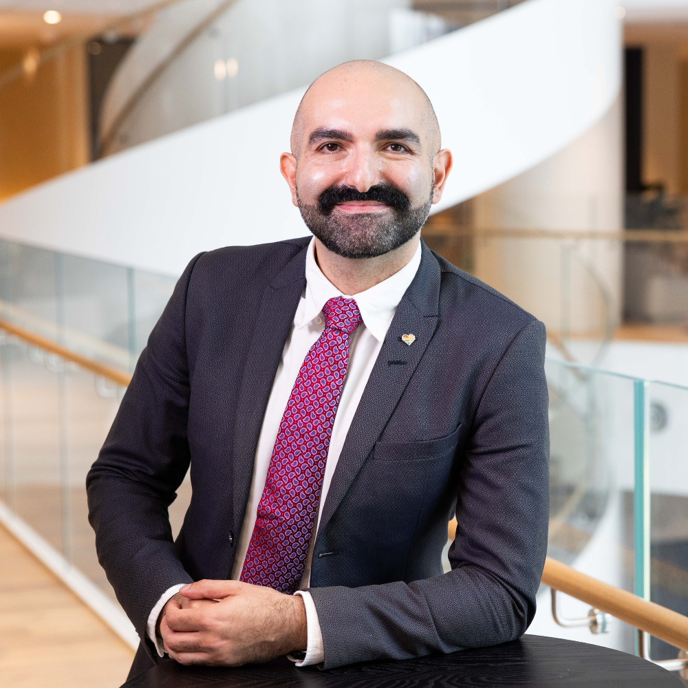 Portrait photo of Arthur Dann looking at the camera with a dark grey suit, white shirt and purple tie