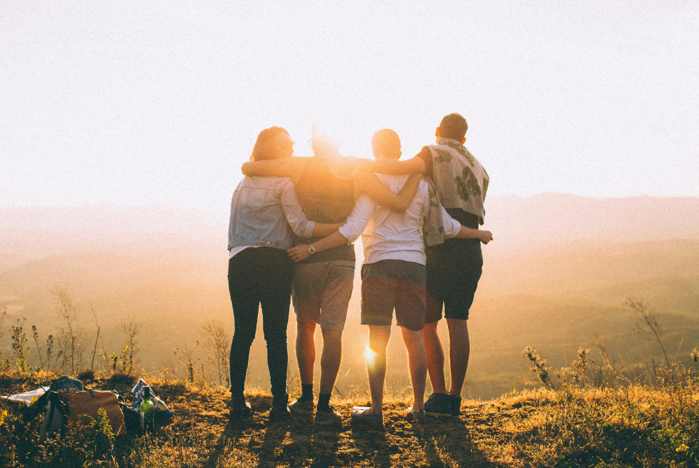 Group of four people with back to camera hugging and looking into sunset