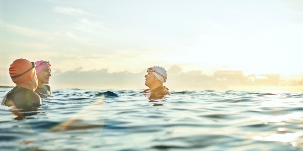 Female friends wearing swimming caps while talking in sea.