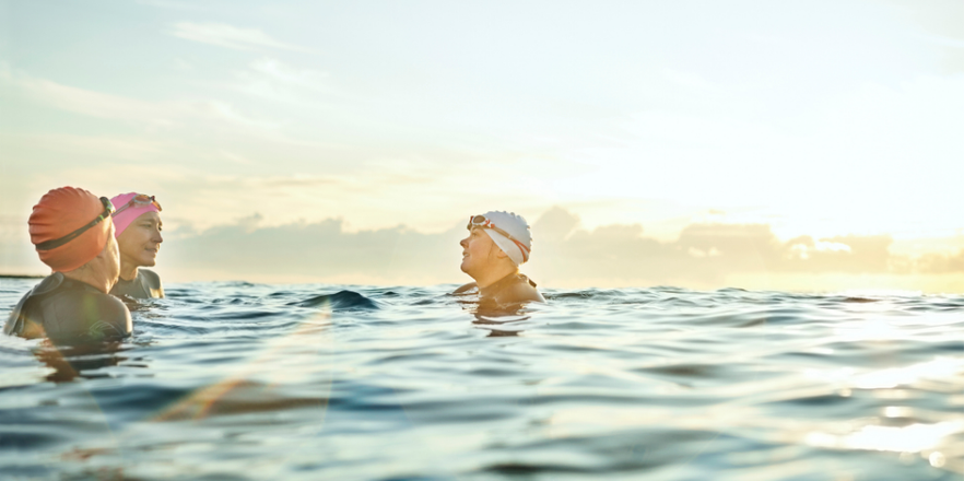 Female friends wearing swimming caps while talking in sea.