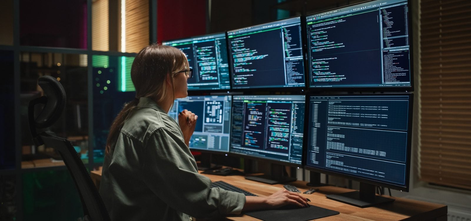 Women working at a desk with multiple screens showing coding.
