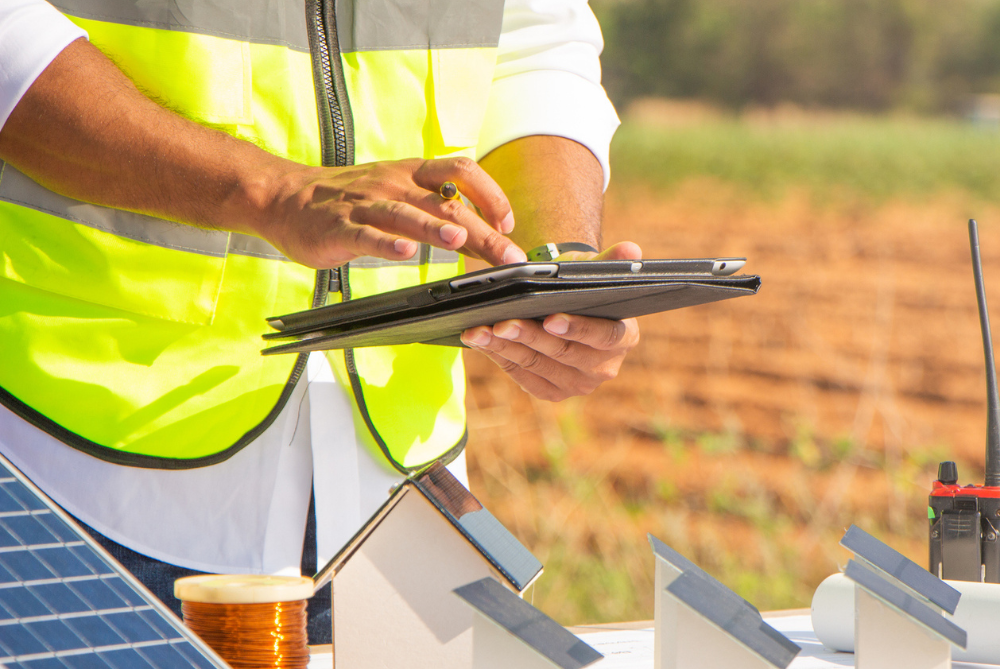Man with high vis vest and white shirt from waist down, holding a laptop working on solar panels 