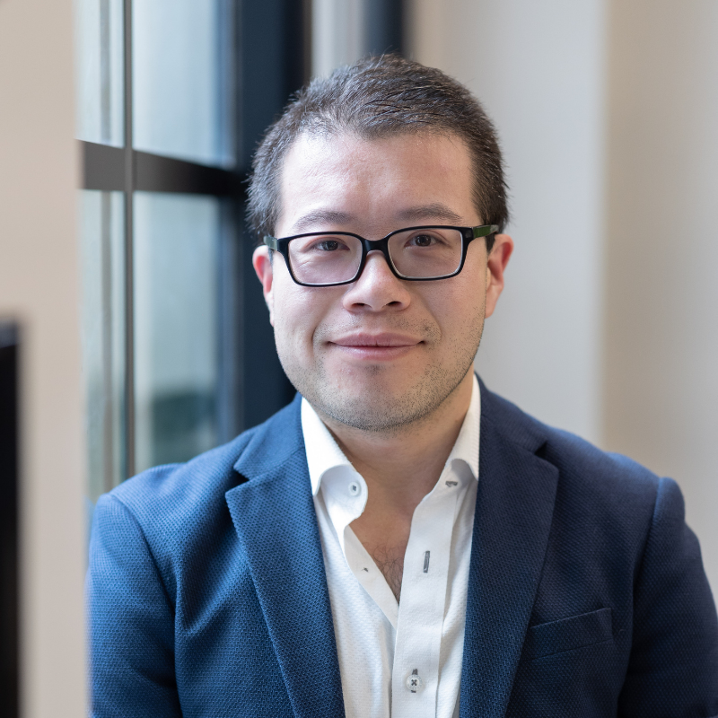 Business man in blue suit with dark hair and glasses looking at camera