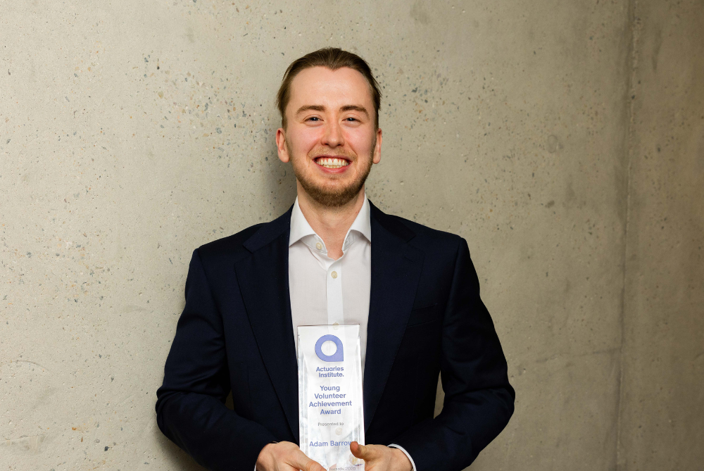 Younger business man with light brown hair and light beard, smiling at camera and holding a clear trophy with blue writing