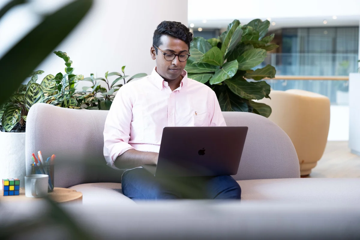 Male in pink business short, looking down and working on computer on lap