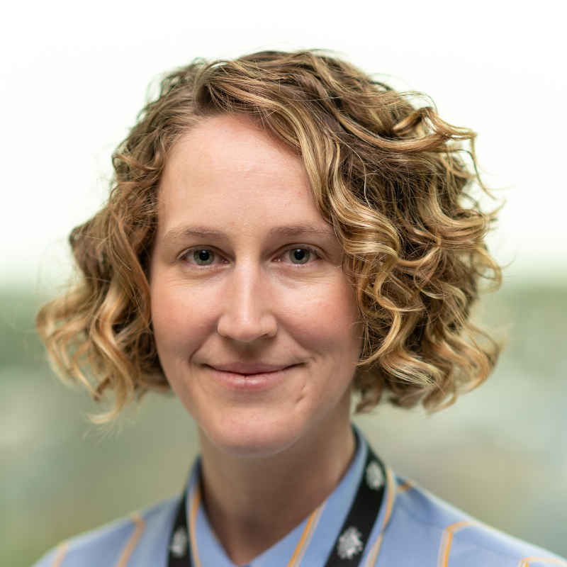 Female with show blonde courly hair smiling and looking at camera.