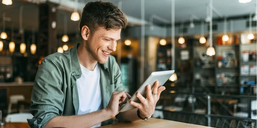 Young man sitting in a cafe reading and using his digital tablet