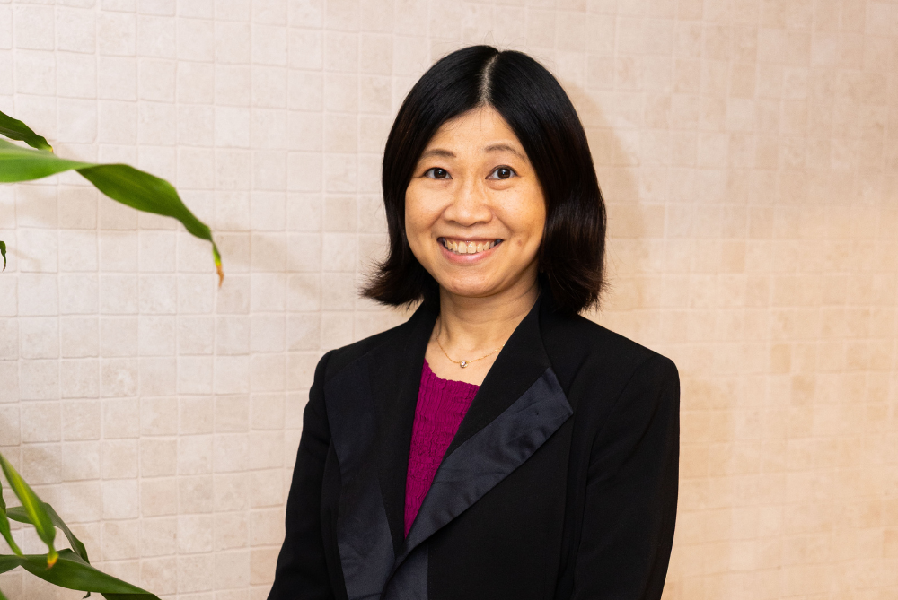 Female with black hair, burgundy top and black jacket smiling at camera