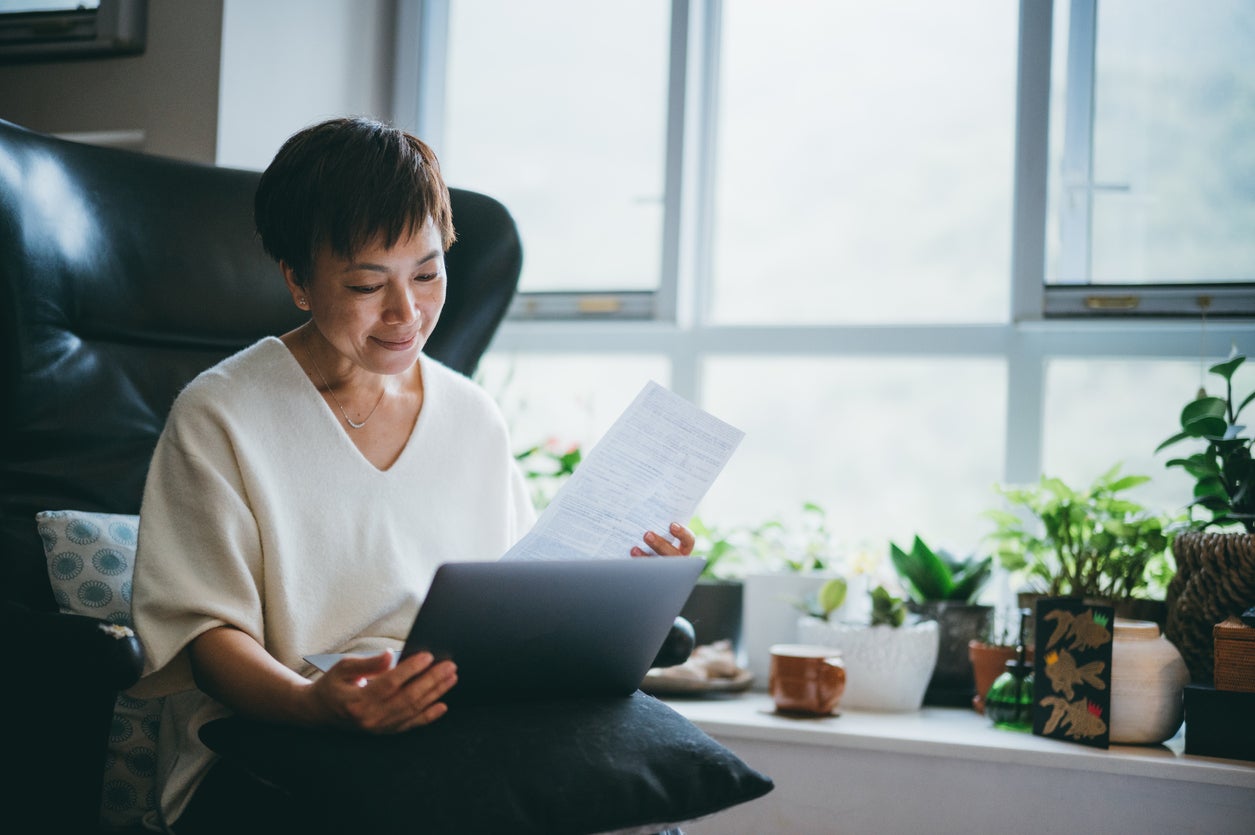 Serious senior Asian woman in checking bills, calculating expenses in front of the laptop computer at home.