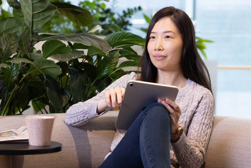 Female sitting on a couch in a mauve jumper and jeans with a ipad