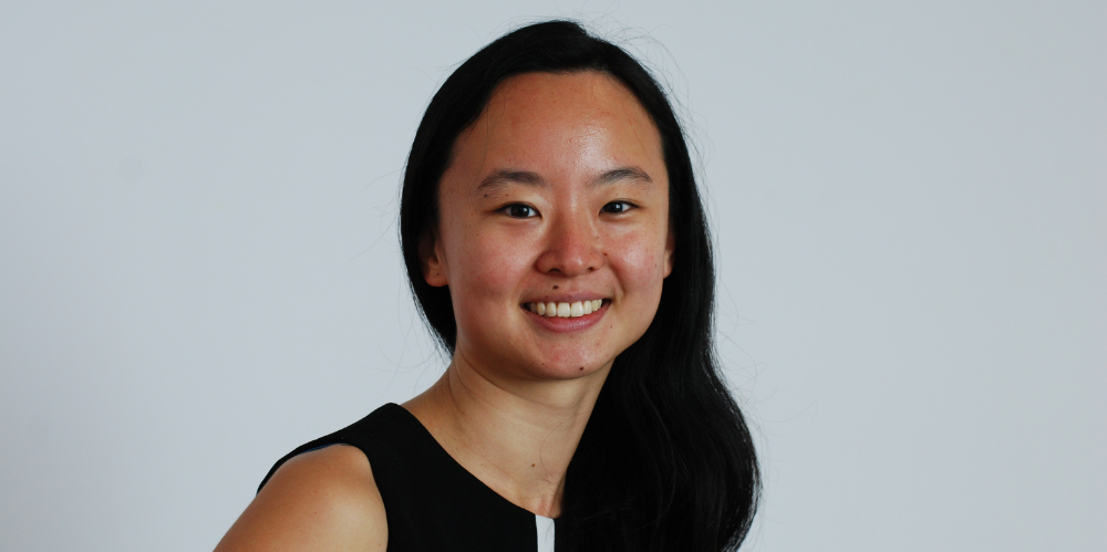 Women in photo smiling at camera with long black hair and black dress white white vertical stripe.