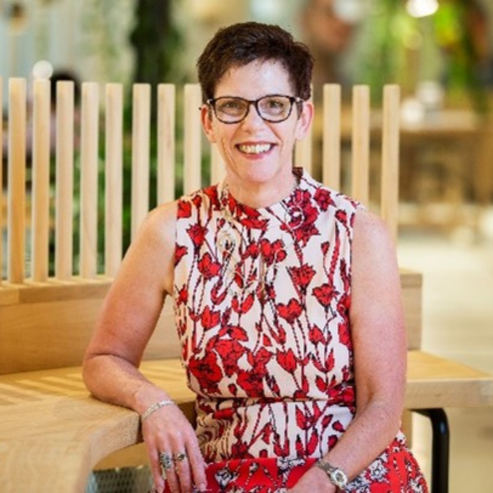 Woman with short dark hair and glasses sits smiling at the camera.