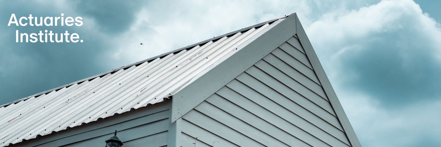 Upwards-looking image of white weatherboard house roof and cloud sky.