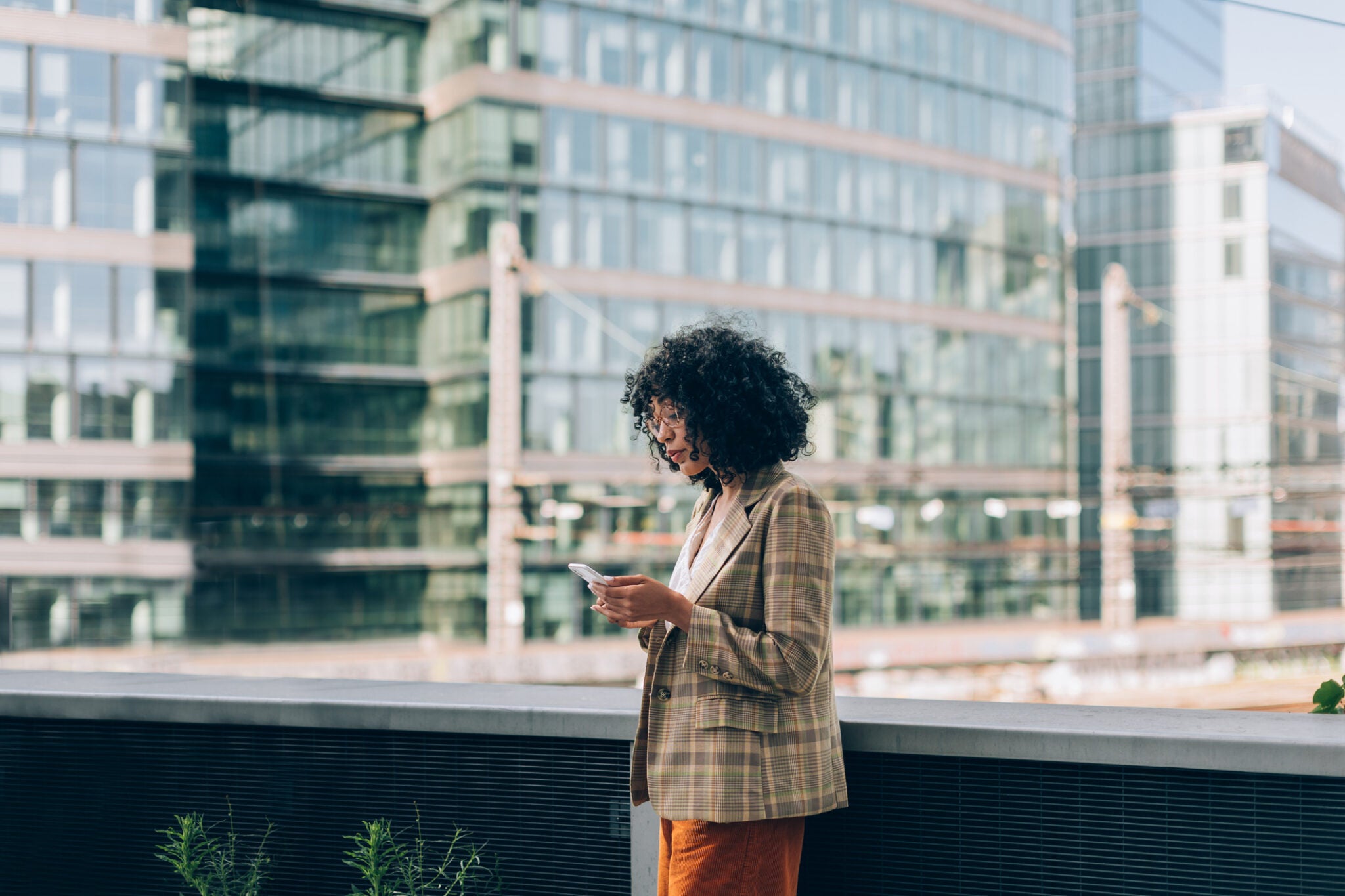 fashion brazilian woman using mobile phone - trendy business working woman under skyscrapers looking at smartphone