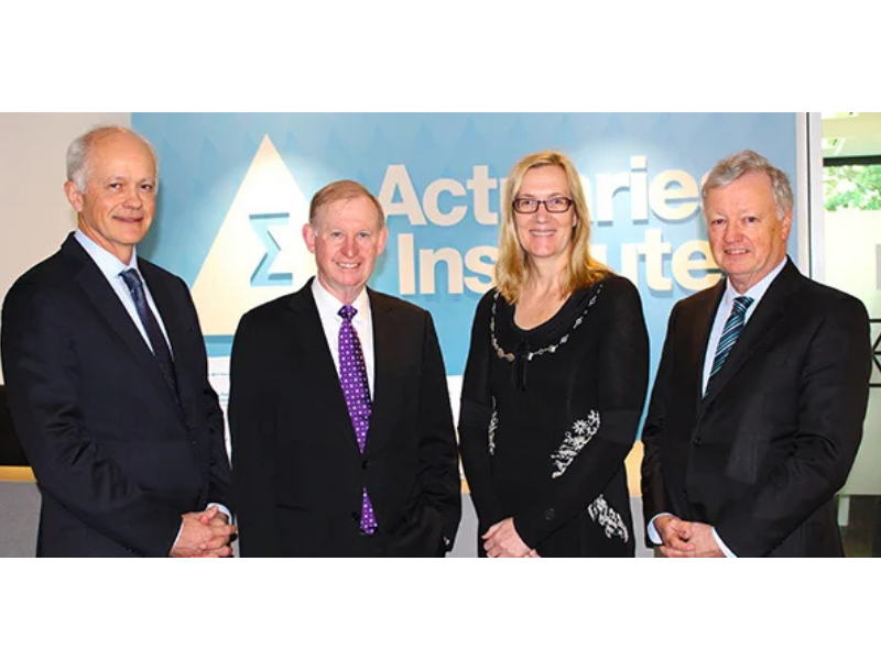 Four people — three men and a woman — stand together in front of an Actuaries Institute branded backdrop.