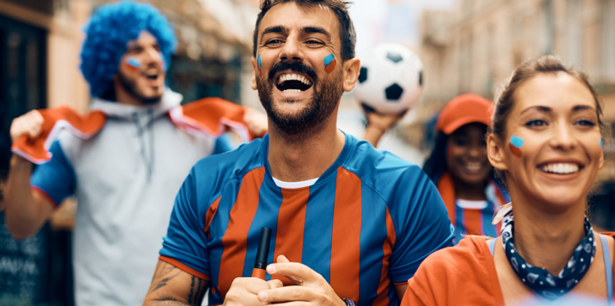 Football fans wearing blue and red striped jerseys celebrating with face paint in a street crowd