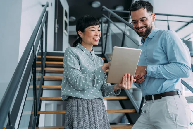 Shot of two colleagues using a digital tablet while walking down stairs in a modern office. Two business people in a motion on stairs in the office.