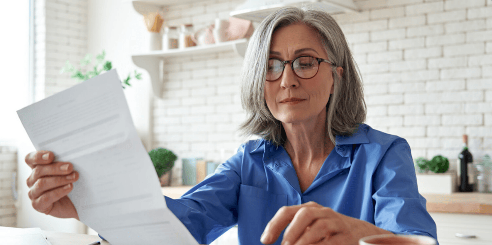 Woman with glasses sitting in kitchen reading important document
