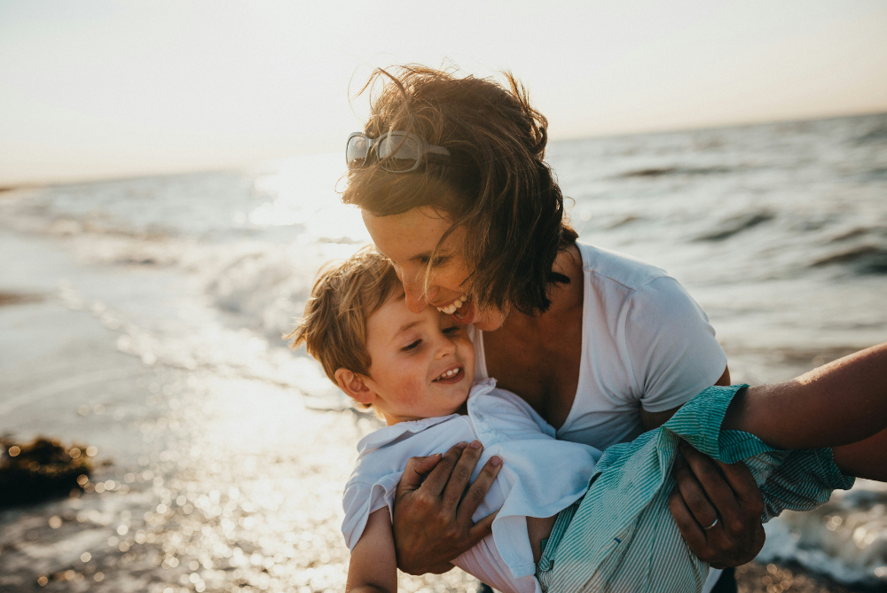 Mother holding young son playing by the ocean