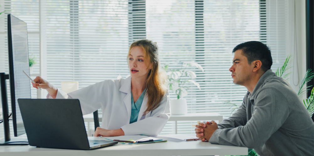 Young female doctor explaining X-ray results to adult male patient during consultation in the clinic office