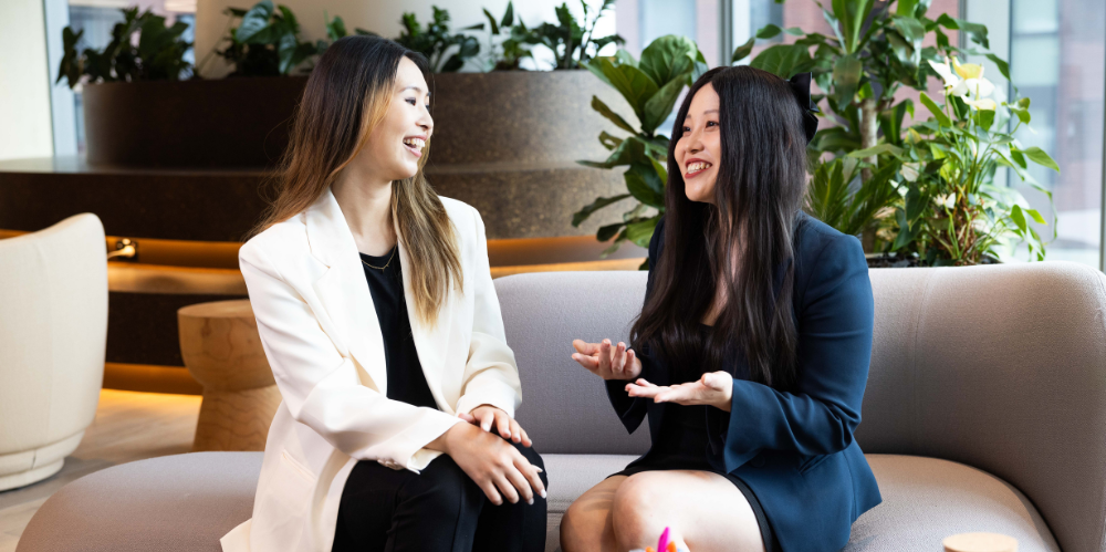 Two professional women sit smiling and talking.