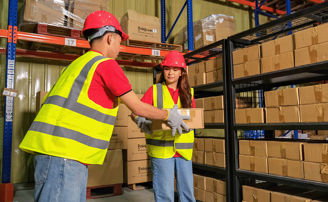 Male worker passing parcel to female worker at the warehouse.