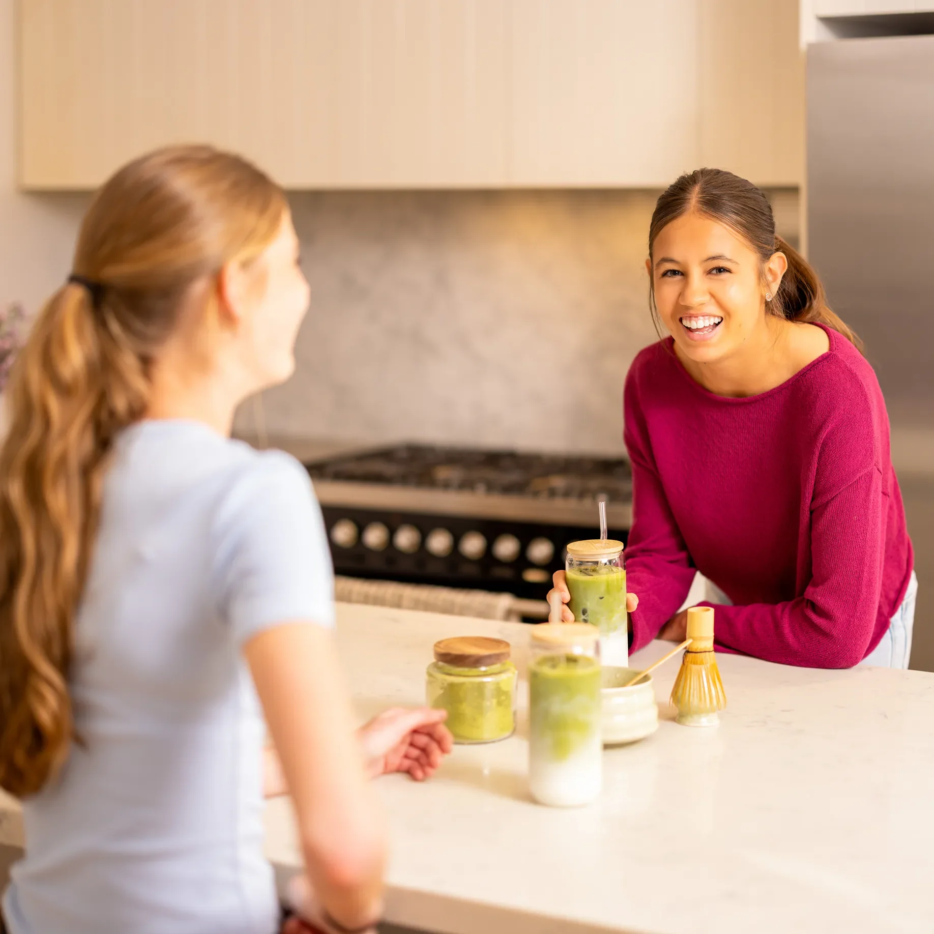 Girl and woman chatting over matcha lattes at a kitchen bench