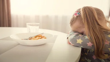 Small child with head down refusing to eat dinner
