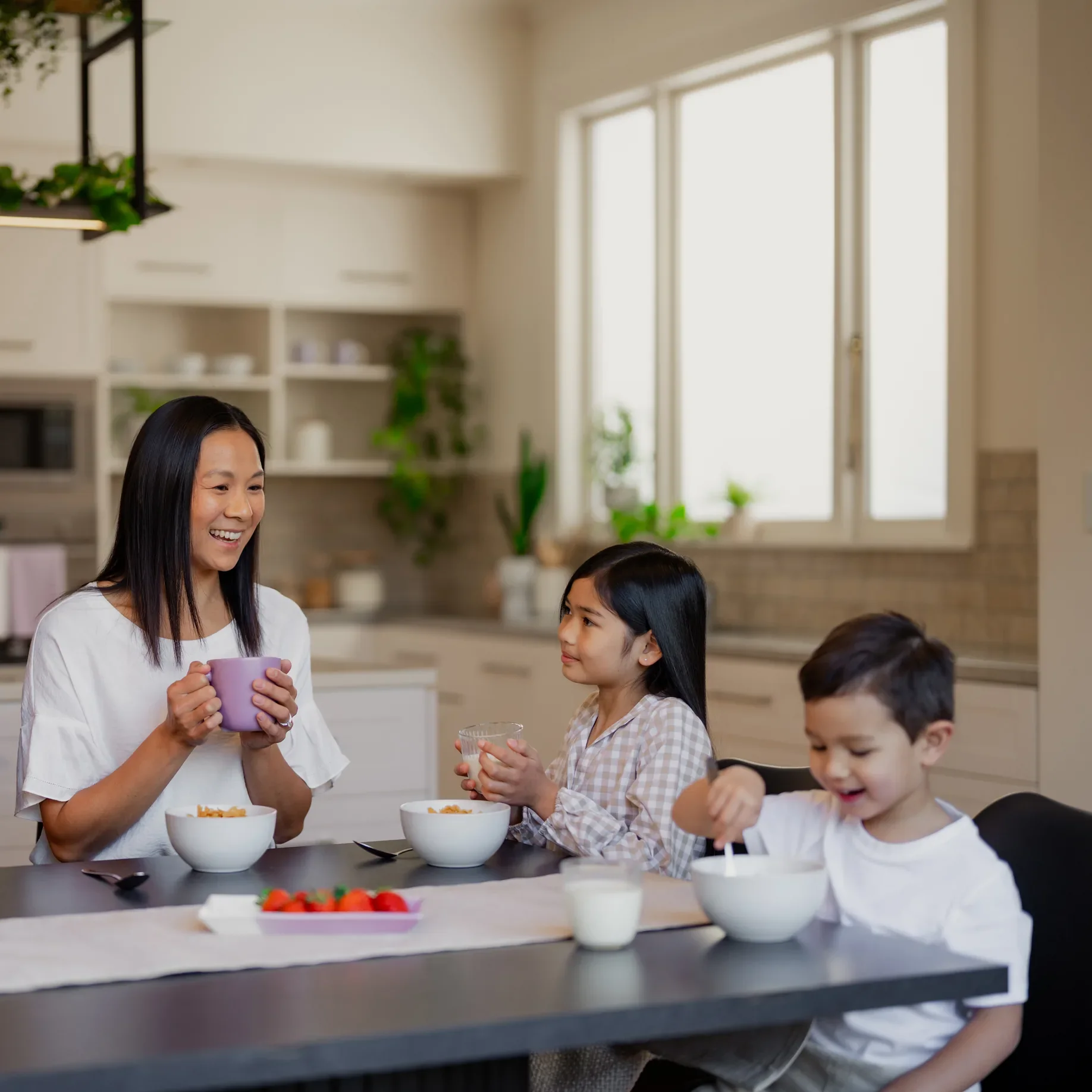 Mother and two children smiling over breakfast at the kitchen table