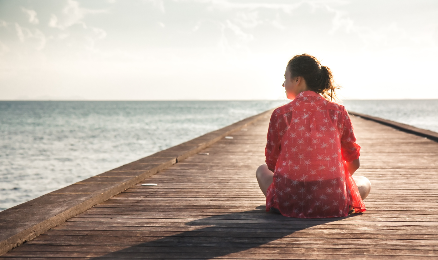 A woman sits at the end of a pier gazing at the ocean, symbolising hope and personal reflection after loss in a tranquil Australian setting.