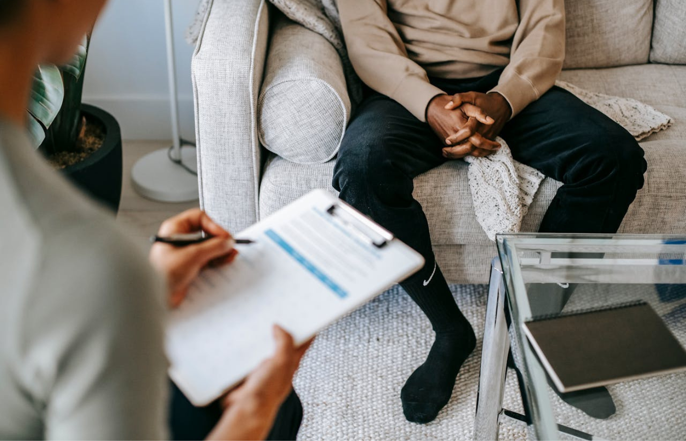 A mid-shot of a man and his doctor. You can see the man's lap over the doctor's shoulder. They are discussing a Mental Health Care Plan. 
