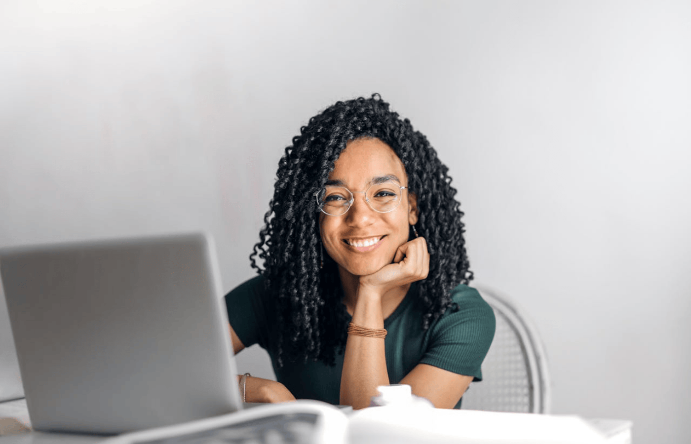 A mid shot of a woman sitting at her desk, using a laptop. She is smiling. 