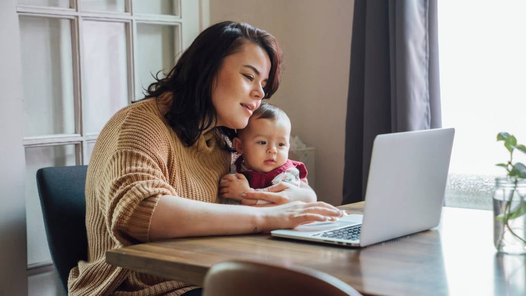 Mother works on her laptop whilst holding her baby