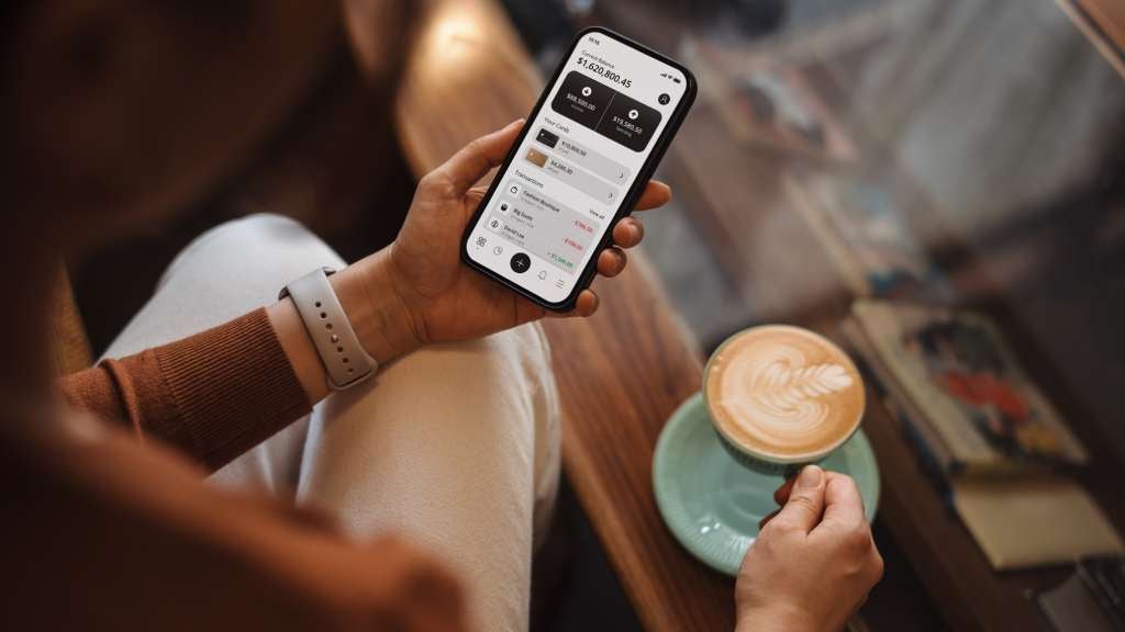 Woman looking at finances on phone while holding a coffee