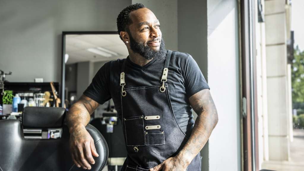 Barber shop owner looking out the window smiling while in thought.