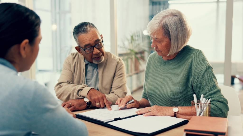 Couple sit at a desk with their lawyer reviewing a legal document before they sign it 