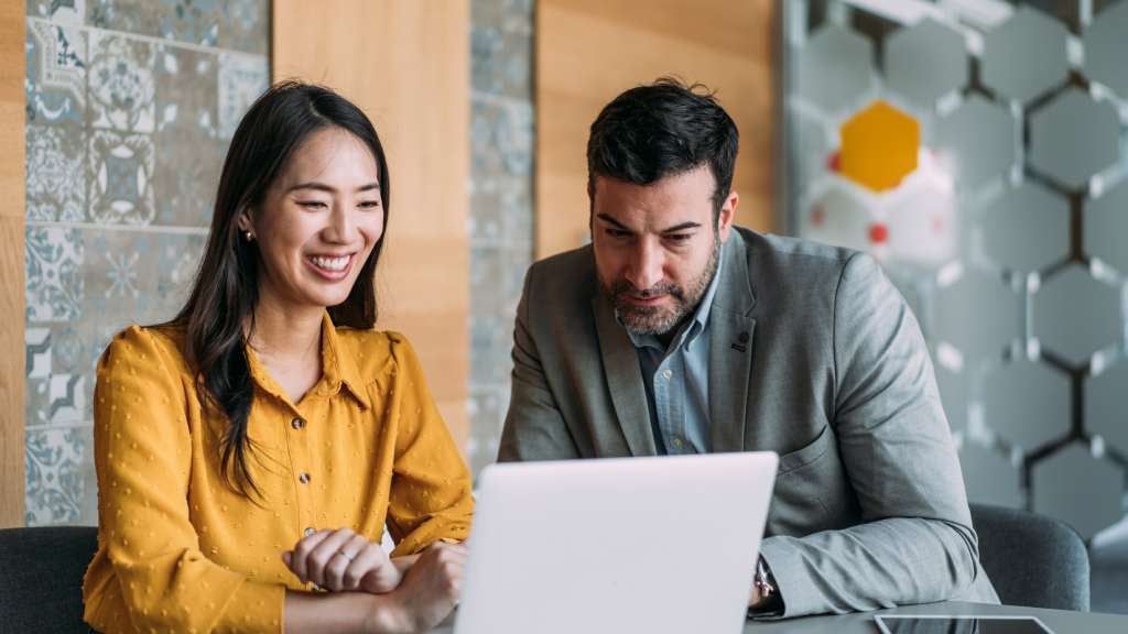 Man and woman sitting at desk looking at laptop.